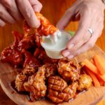 Delicious chicken wings on a wooden platter with dipping sauce and carrot sticks.