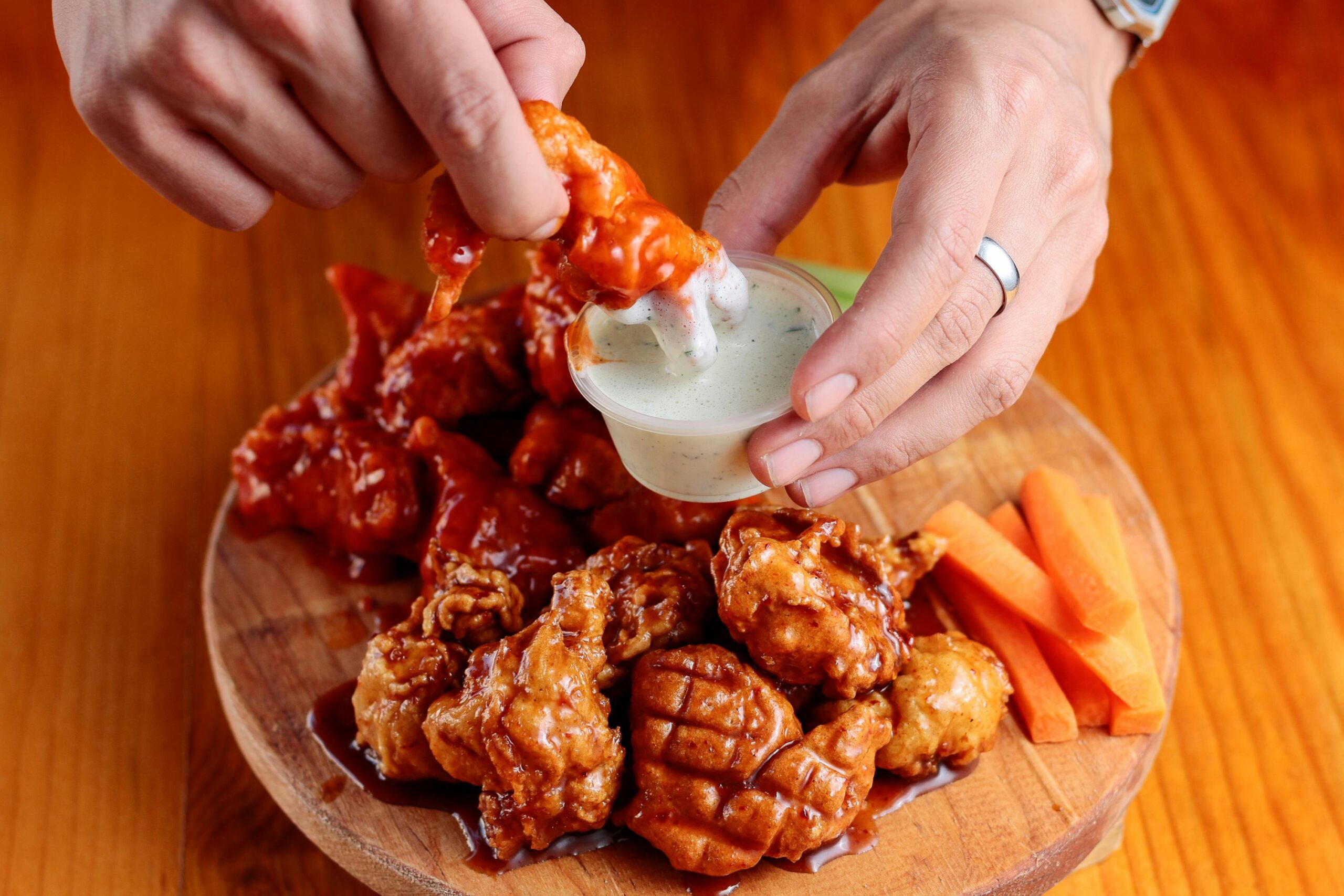 Delicious chicken wings on a wooden platter with dipping sauce and carrot sticks.